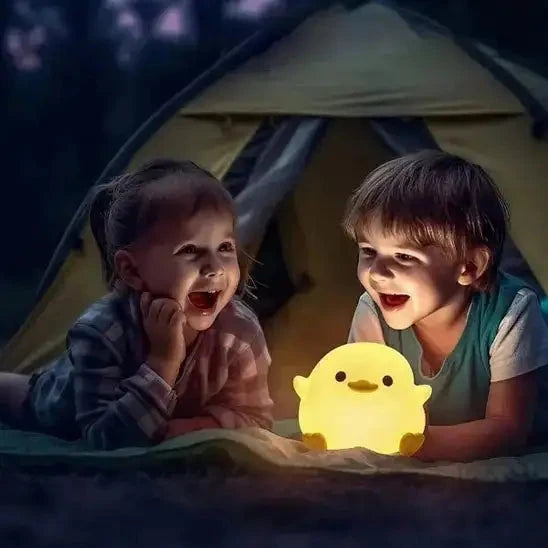 Deux enfants souriants dans une tente, éclairés par une veilleuse en forme de canard jaune posée devant eux