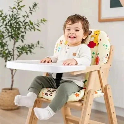 Jeune enfant souriant assis dans une chaise haute en bois, sur un coussin clair à motifs colorés