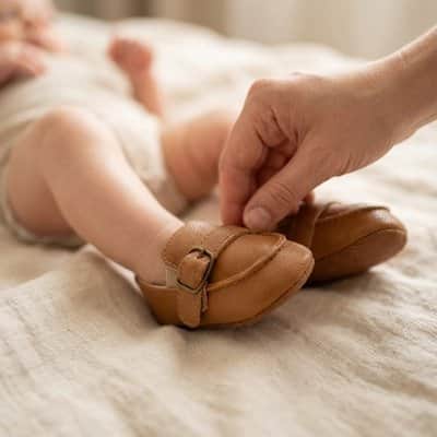 Main ajustant une chaussure marron clair sur le pied d’un bébé allongé